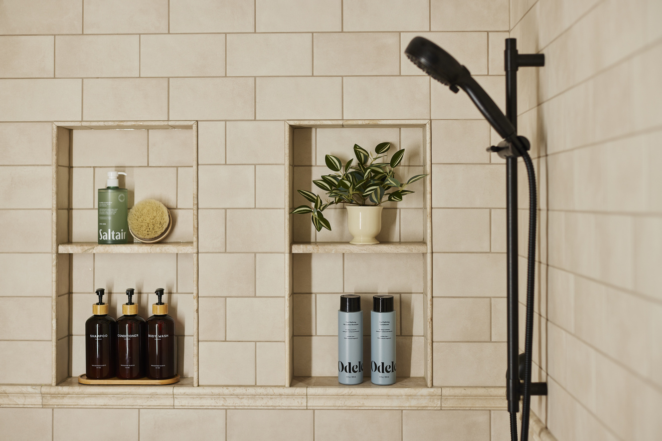 Beige tiled shower with two recessed storage niches, built-in shelves, and a dark handheld showerhead in a Blaine bathroom remodel.